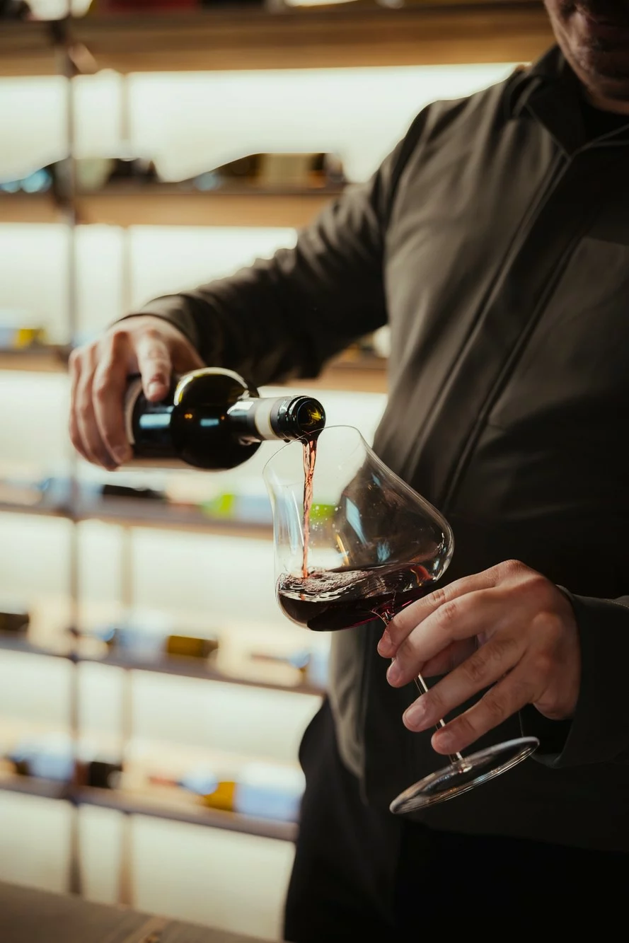 Sommelier versa vino rosso all'interno di un calice inclinato.