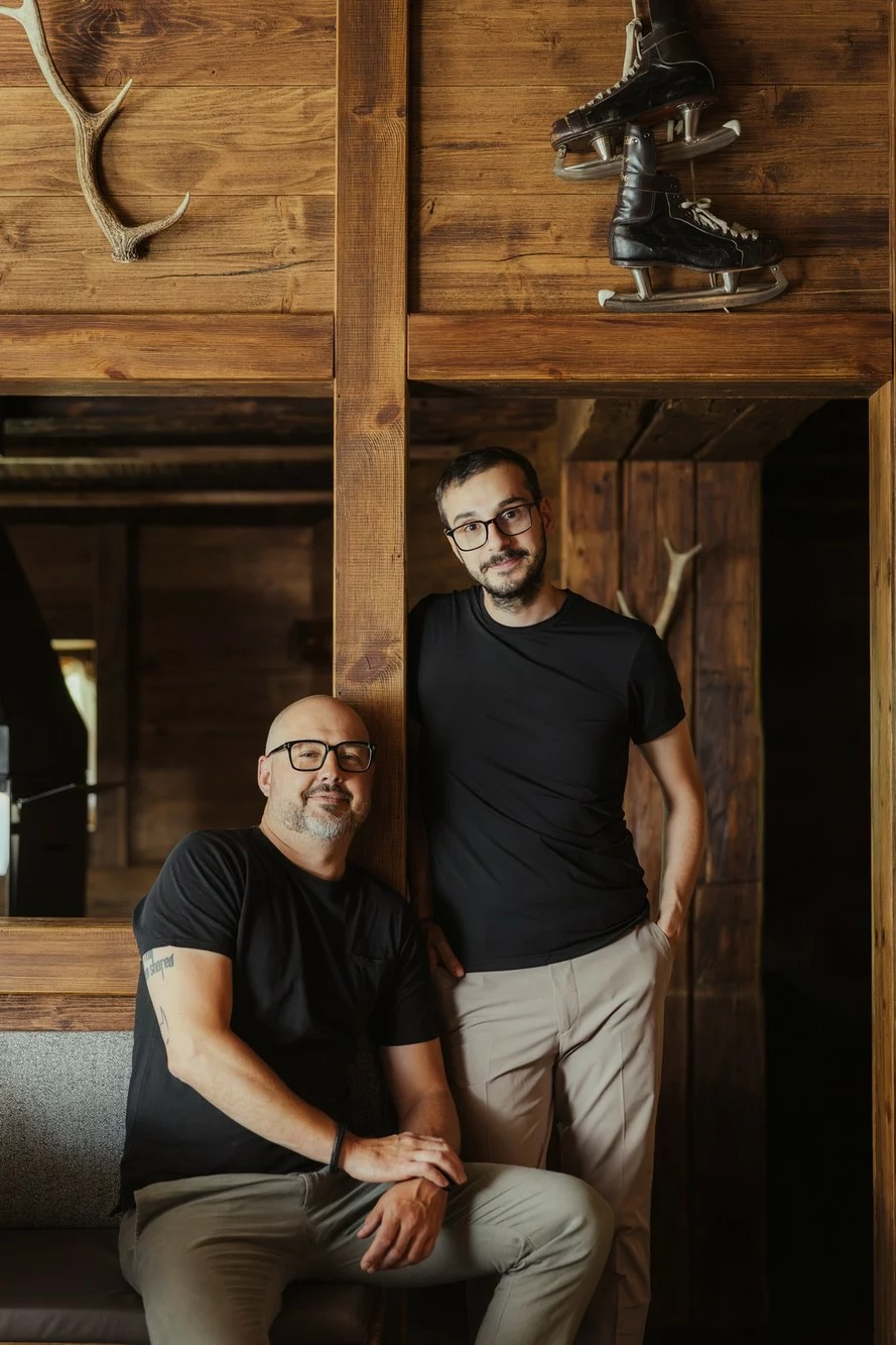 Ritratto di Michel Oberhammer e Federico Rovacchi con parete in legno con palco di cervo e pattini da ghiaccio.