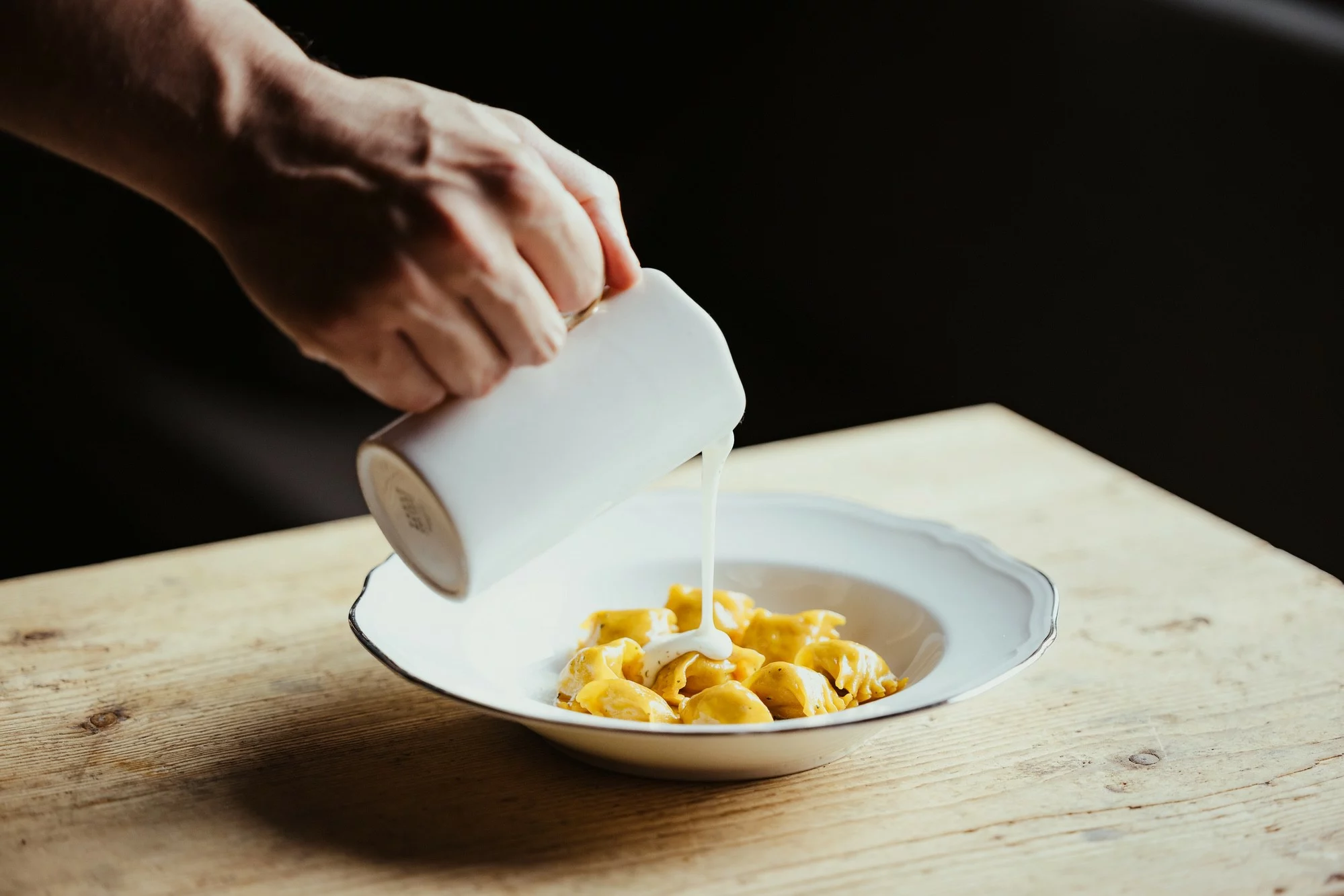 Mano versa panna su piatto di tortelli freschi.